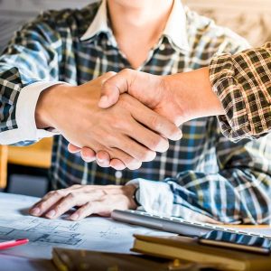 Men in Plaid Shirts Shaking Hands with Blueprints on Table